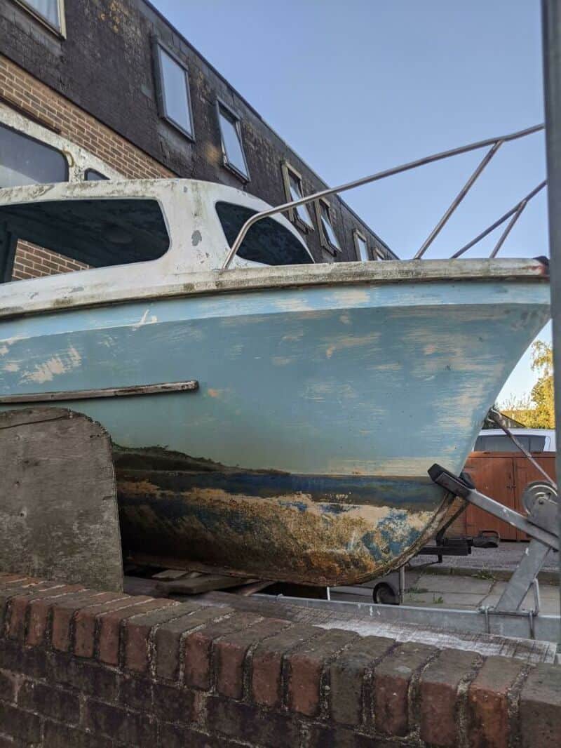 Old boat with worn paint and algae, on a brick platform outside a building.