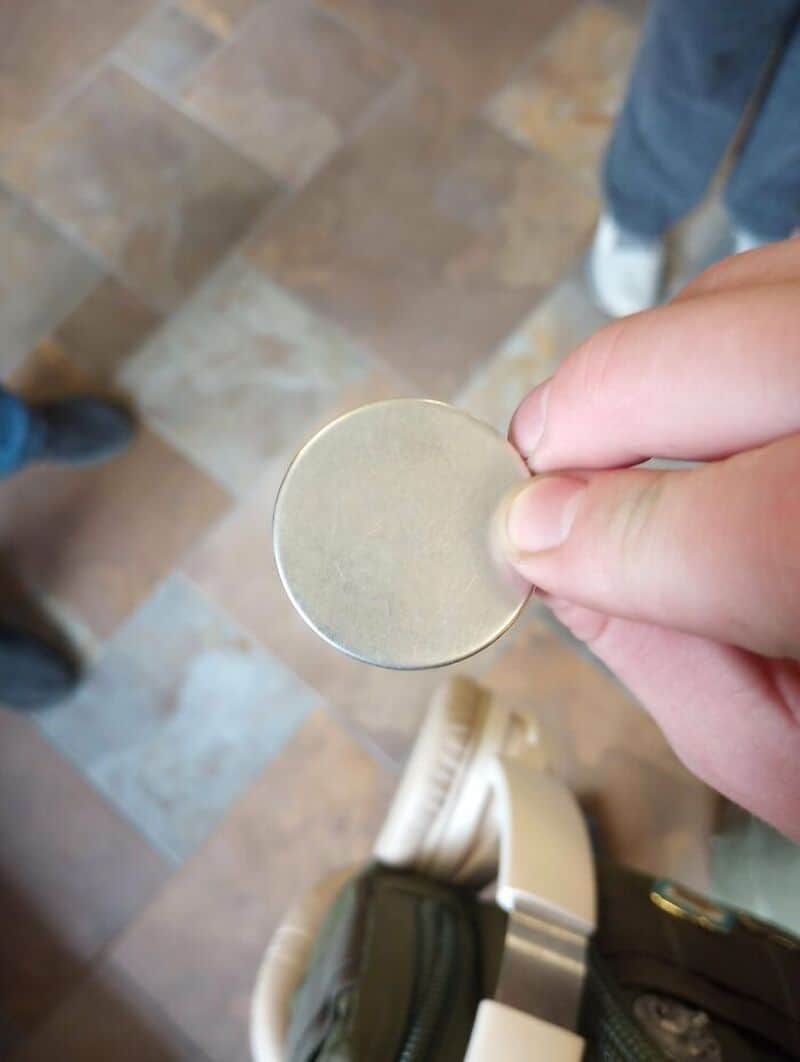 Person holding a round, flat, shiny object with a tiled floor in the background.