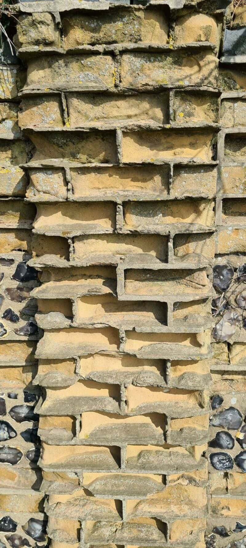 Stack of old, weathered bricks with some black stones in between.