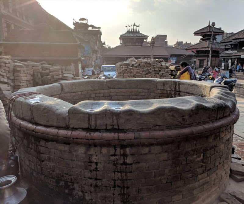 Ancient circular brick structure with stone top in a busy outdoor market area.