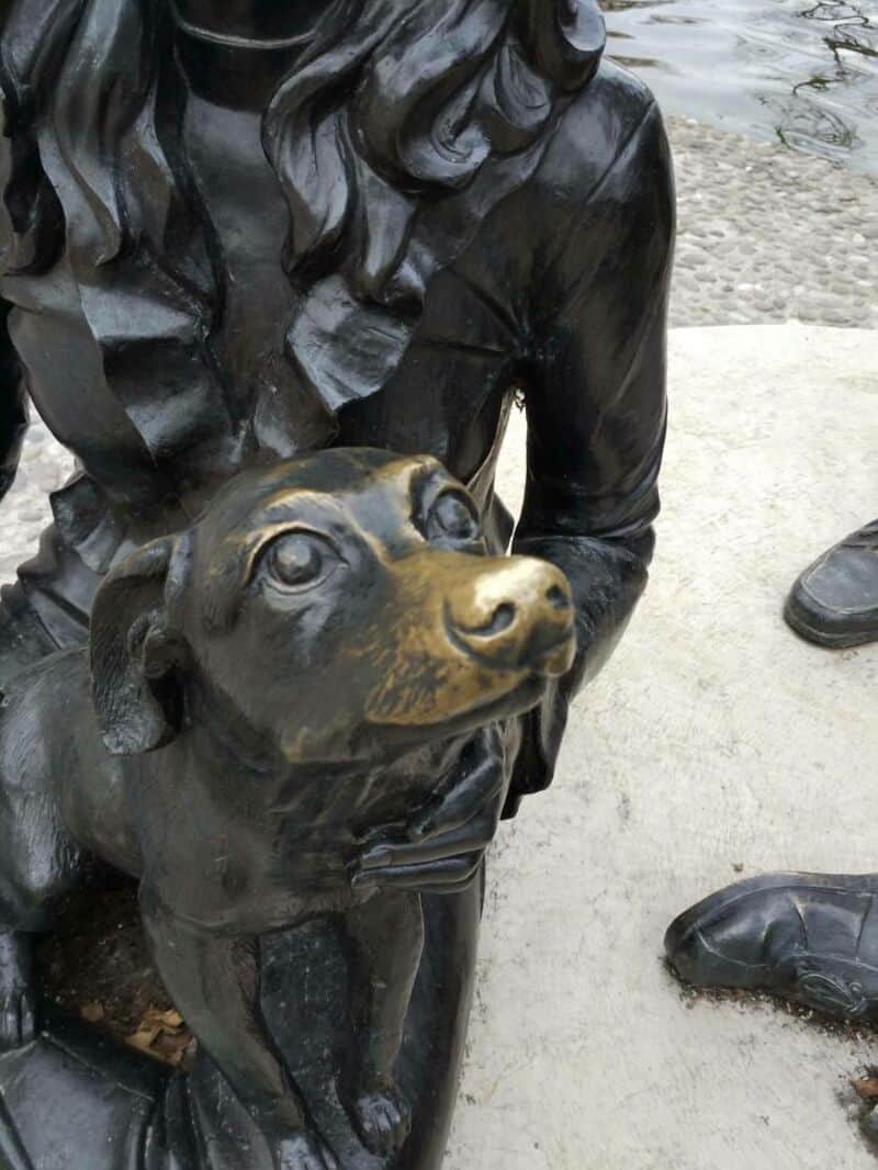 Bronze statue of a girl with a dog, part of a public art display.