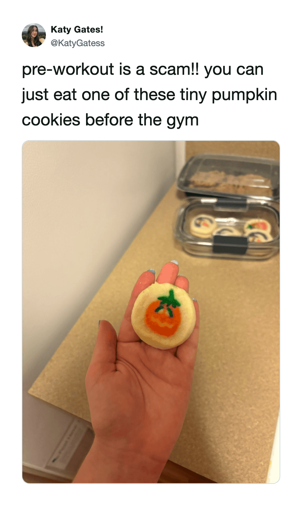 Tiny pumpkin cookie with green stem and orange face, held in hand.