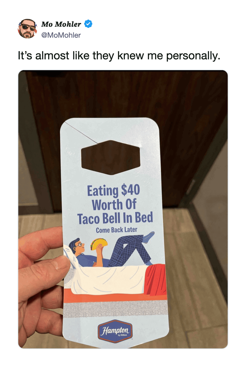 A person holding a Hampton Inn key card with a humorous message about Taco Bell.