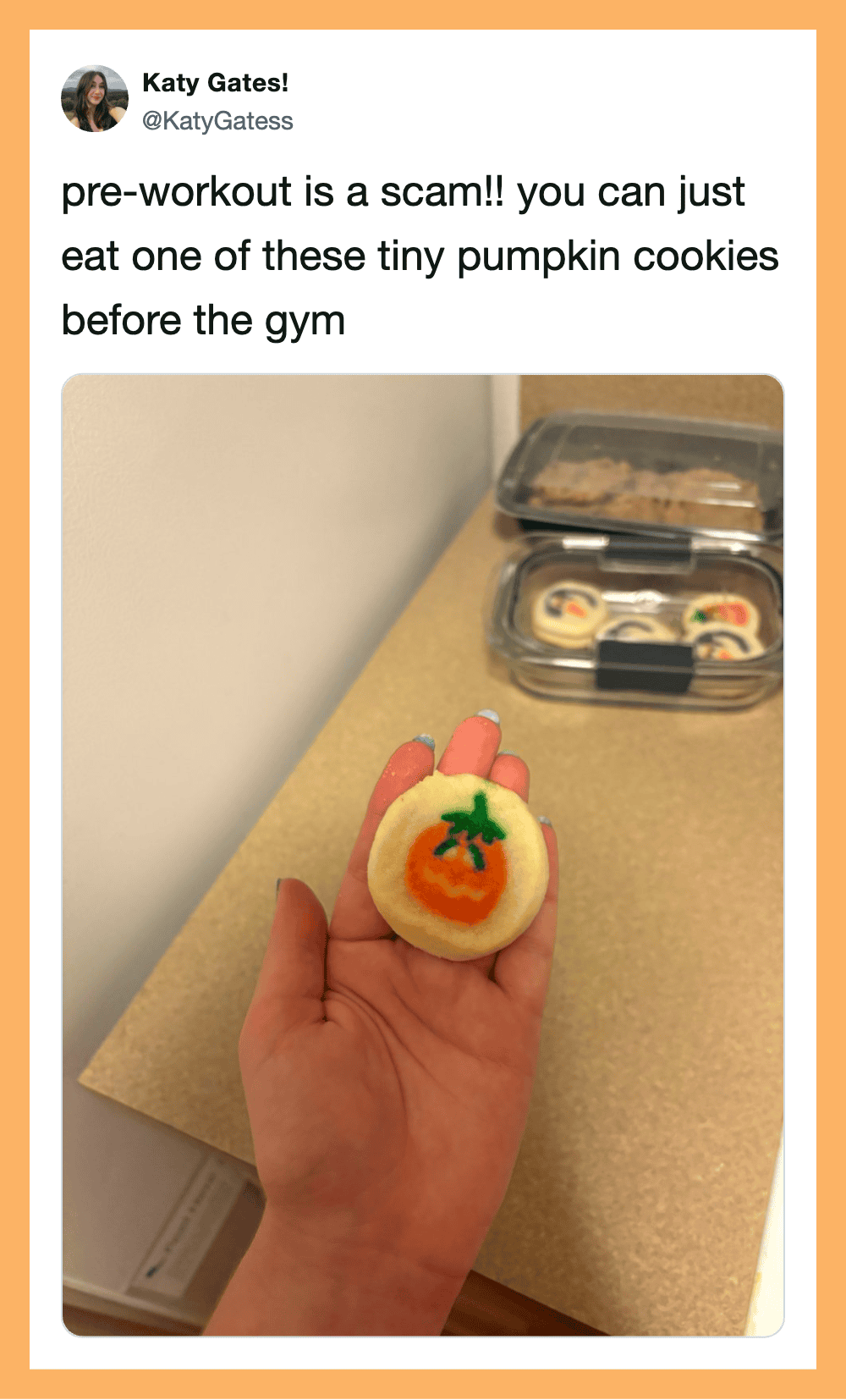 Person holding a tiny pumpkin cookie with a green stem and orange pumpkin face.