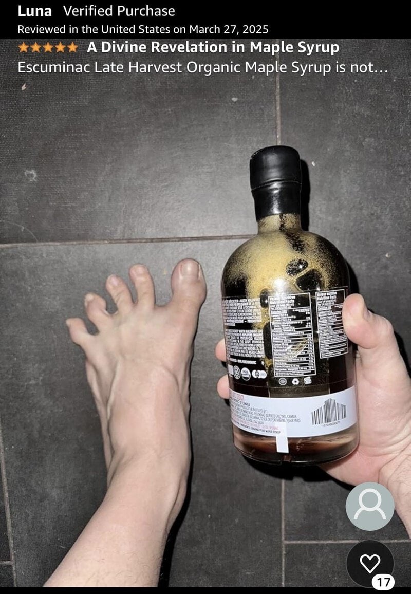 Hand holding a maple syrup bottle next to a foot on a tiled floor.