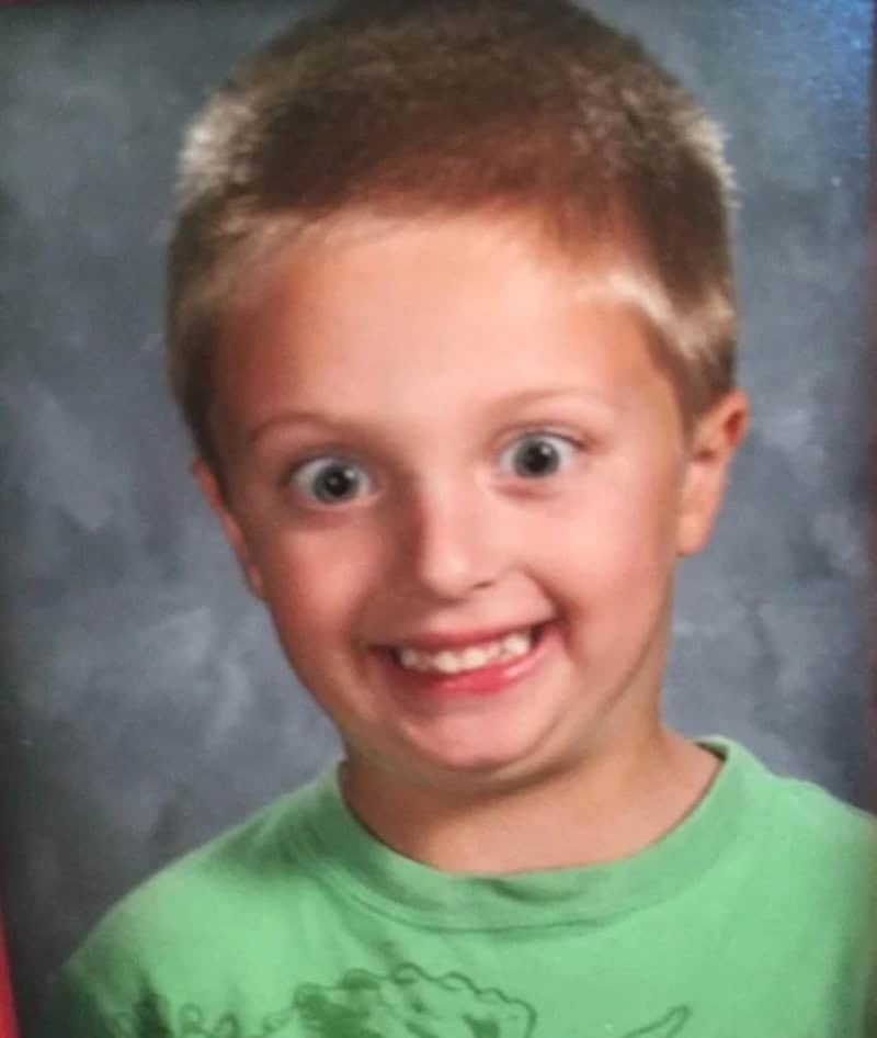 A young boy with short light brown hair, wide eyes, and a big smile, wearing a green shirt.