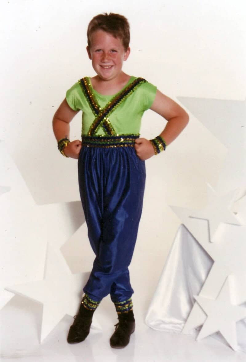 Child in bright green and blue costume with stars around, smiling.
