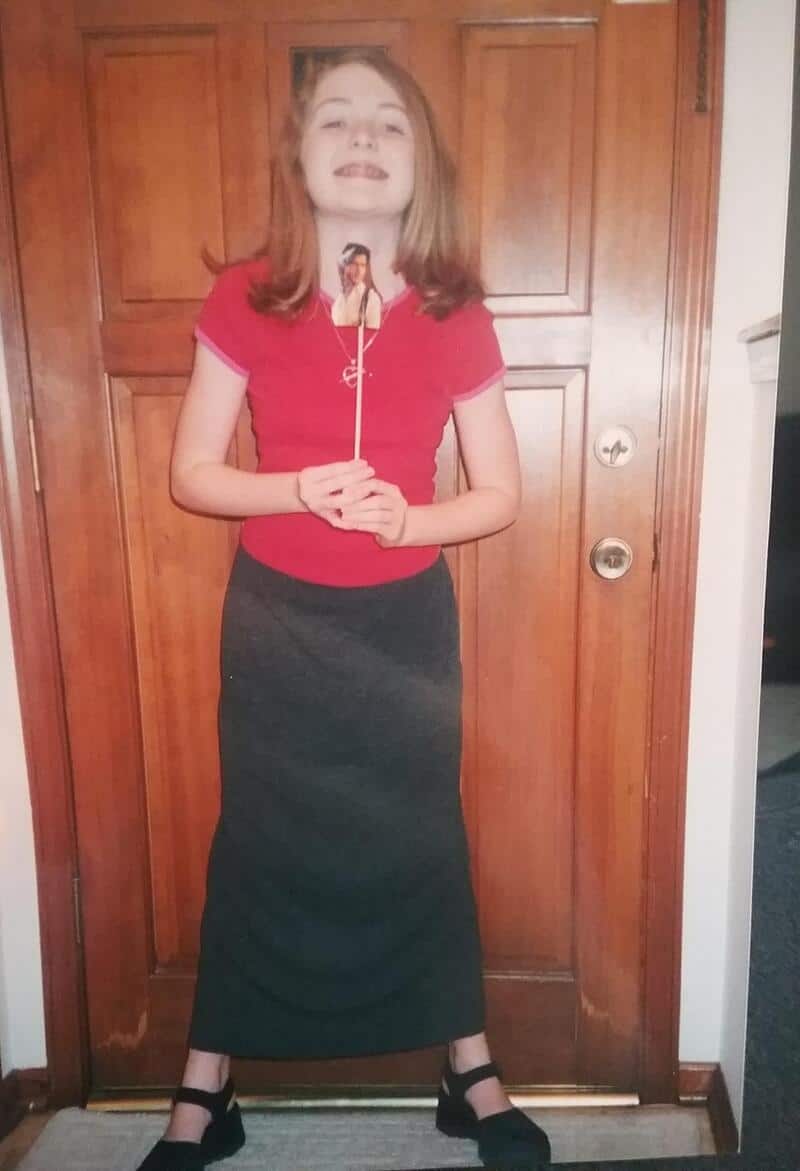 Girl with long hair in a red top and black skirt holding a selfie stick.