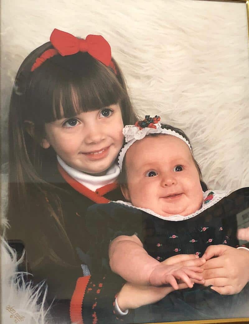 Two young girls, one older with a red bow and the other younger with a headband, smiling.