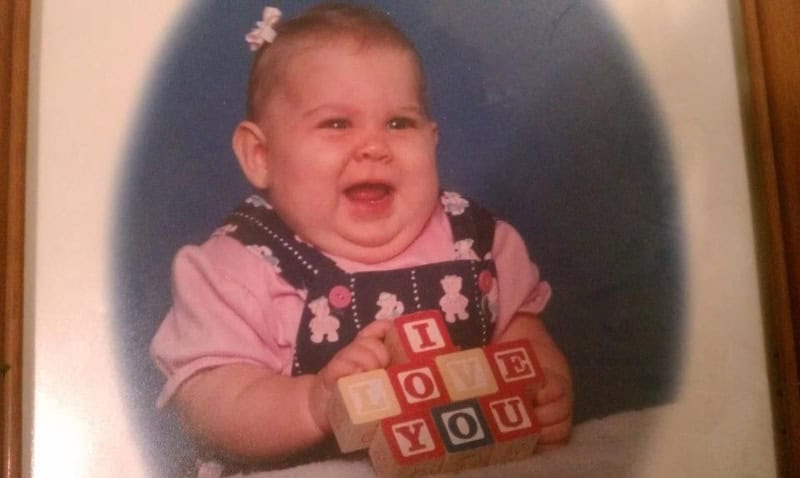 Baby girl with a big smile holding wooden blocks spelling 'I LOVE YOU'.