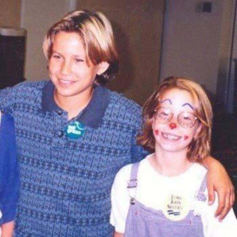 Two kids, one with a blue sweater and the other with face paint, smiling together.