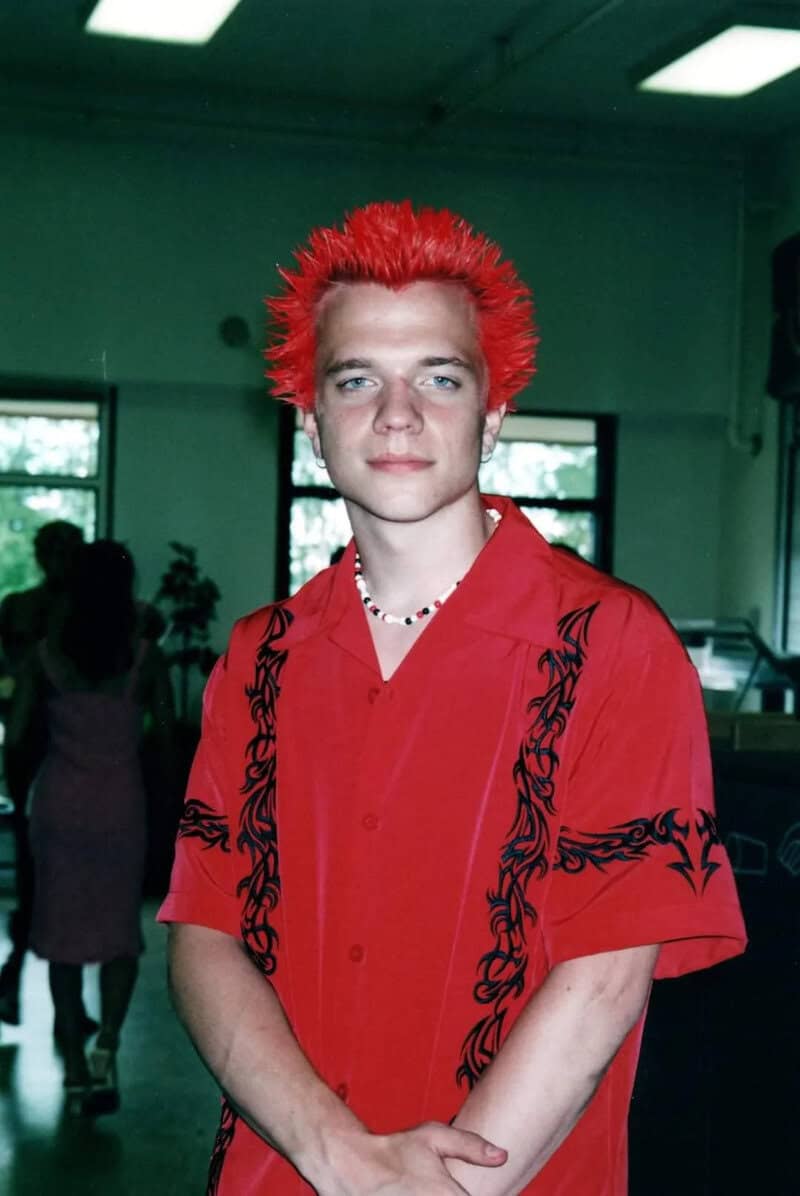 Young man with bright red spiked hair wearing a red shirt with black designs.