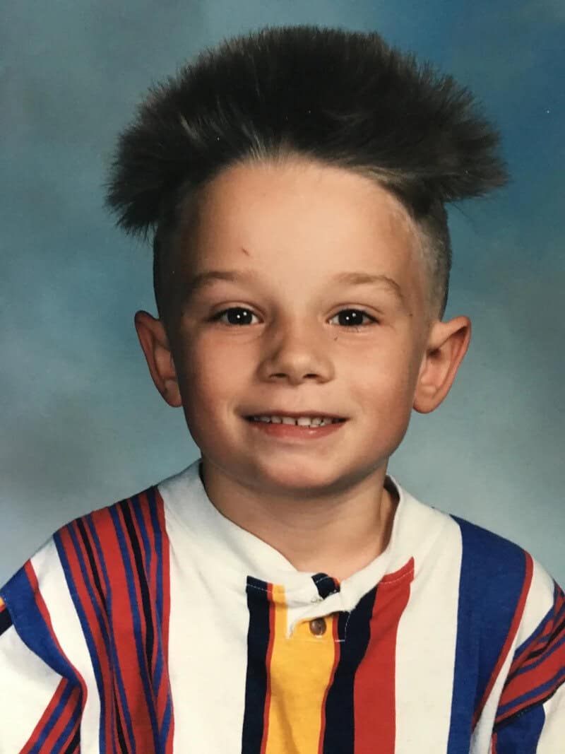 Child with a big, fluffy hairstyle, smiling, wearing a colorful striped shirt.