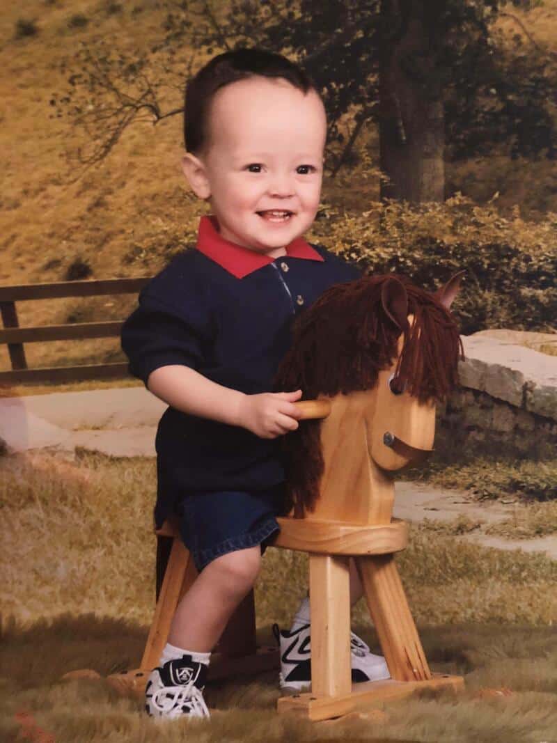 Smiling young boy riding a wooden hobby horse outdoors in a park.