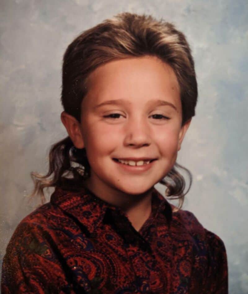 Young girl with brown hair and a big smile, wearing a patterned shirt.