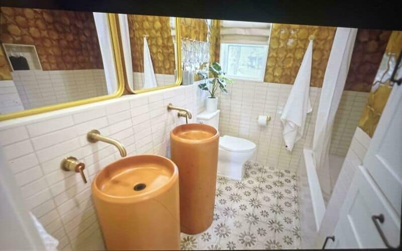 Bathroom with two orange sinks, a toilet, and a window with plants.