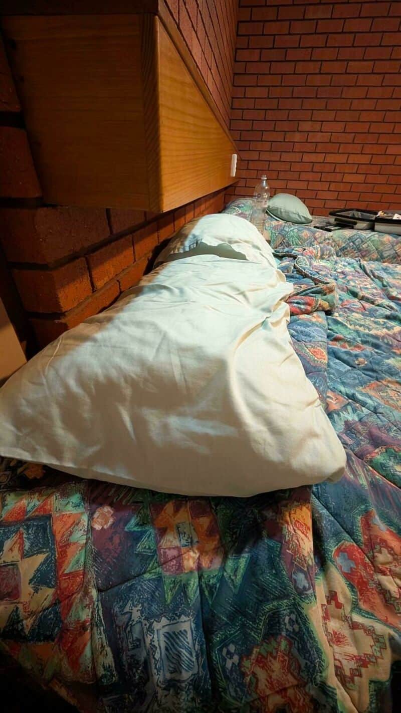 Pillow and blanket on bed with a brick wall and wooden headboard.