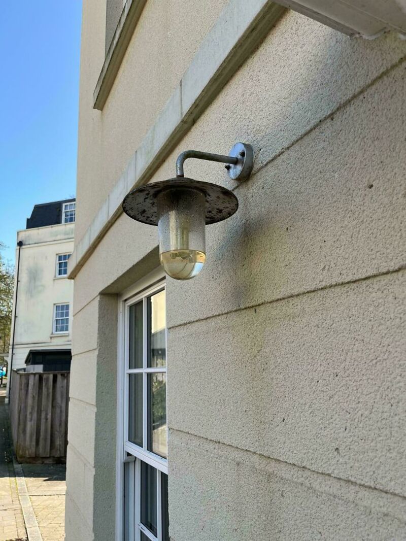 Outdoor wall light fixture with a broken glass cover and a bent arm.