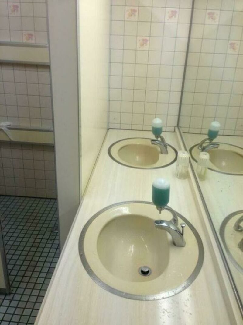 Bathroom sink with a soap dispenser on the faucet, mirror reflecting the sink.