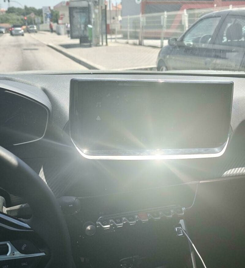 Car dashboard with a blank screen and sunlight glare, view from driver seat.