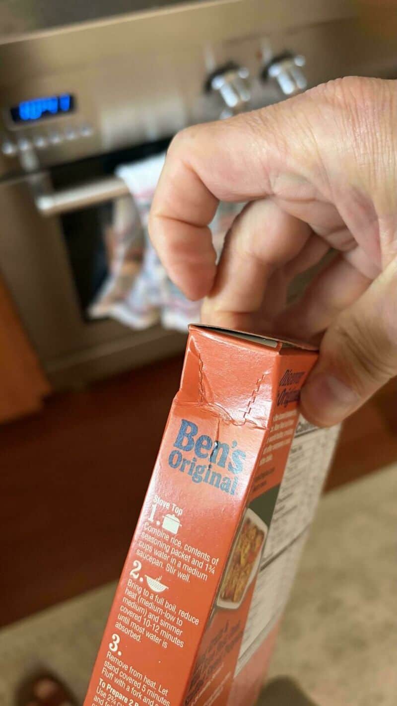 Hand holding a box of Ben's Original rice near a dishwasher.