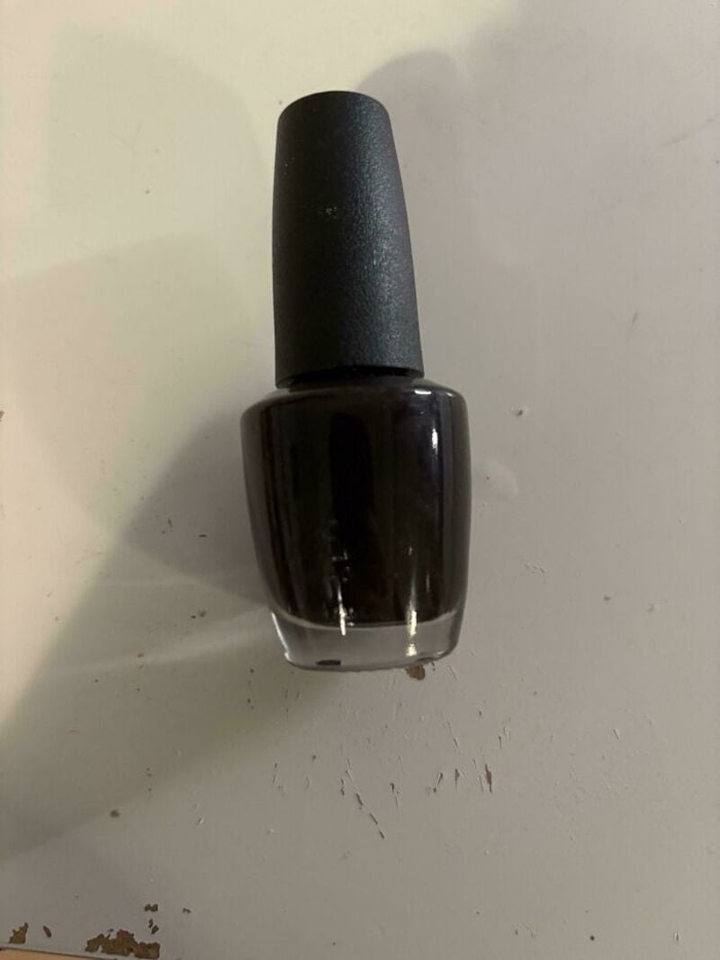 Black nail polish bottle with a black cap on a white surface.