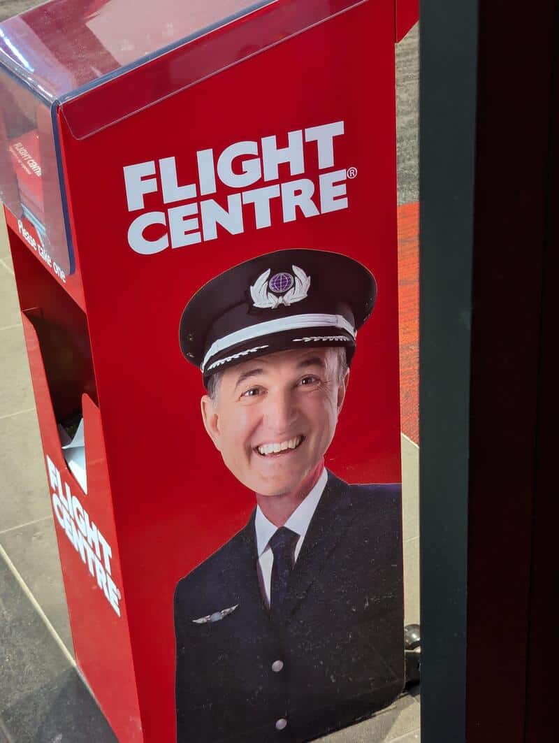Flight Centre advertisement featuring a smiling man in a pilot uniform on a red background.