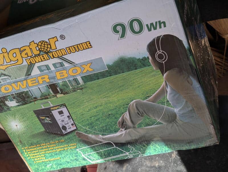 Woman wearing headphones sits on grass next to a portable power box, with a generator unit in the EB.