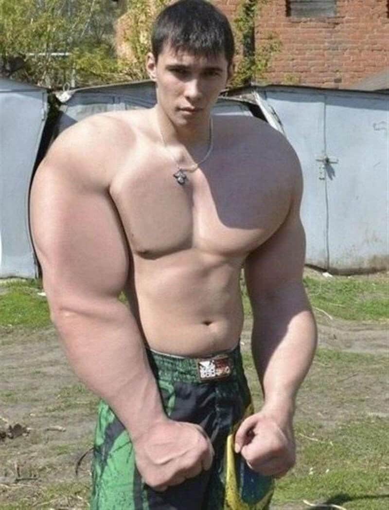 Young shirtless man with muscular build standing outdoors, fists clenched, wearing green camouflage-.
