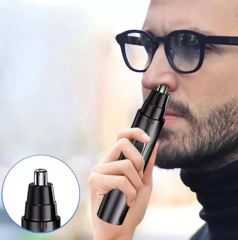 Man using an electric nose trimmer, black device near nostril, close-up with accessory zoomed in.