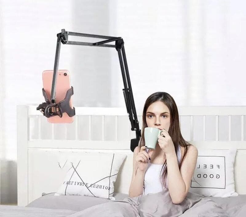Woman in bed using a mounted smartphone arm for filming; sipping from a mug.