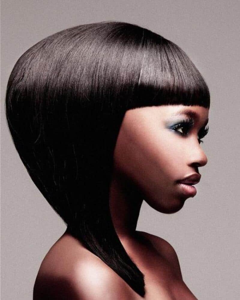 Side profile of a woman with a geometric black bob hairstyle and bold makeup.