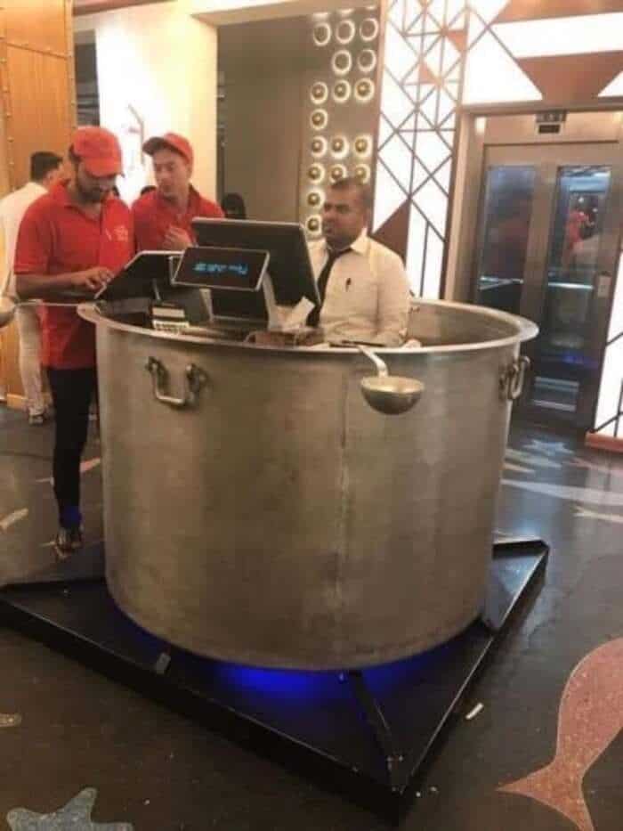 Man sitting inside a large metal pot at a restaurant with staff around.