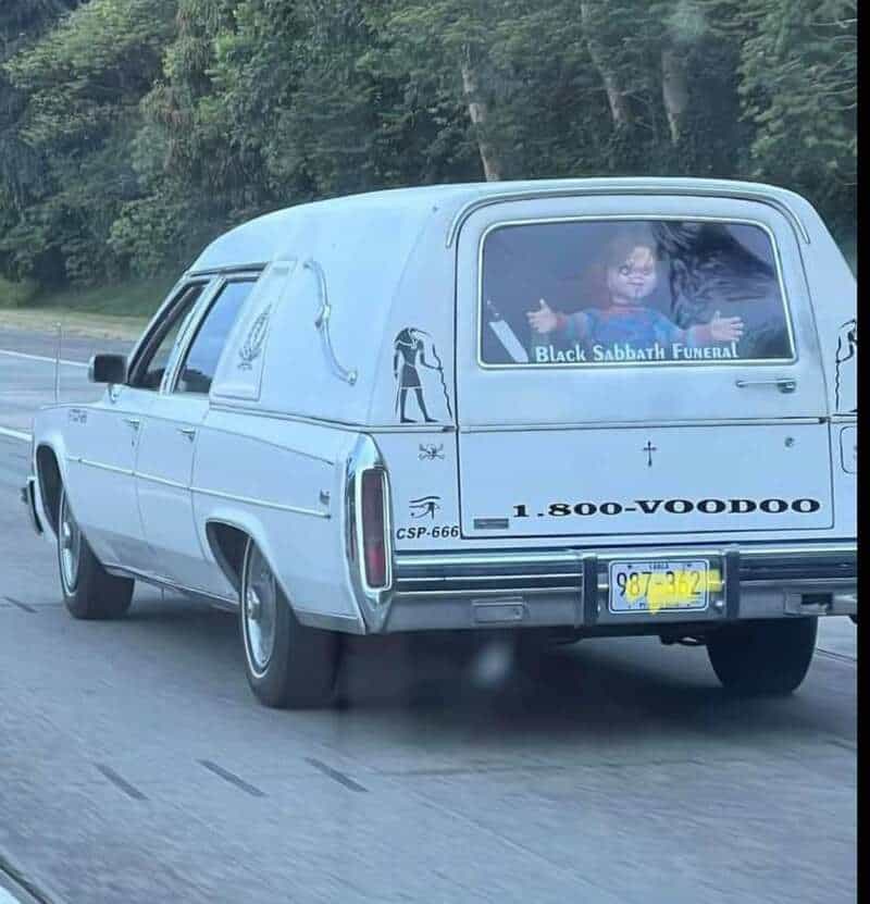Hearse with a Black Sabbath Funeral sign and a person giving a thumbs up inside.