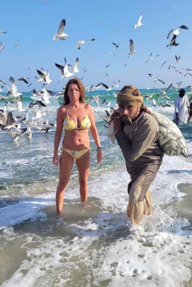 Woman in yellow bikini standing in ocean with seagulls flying around her.