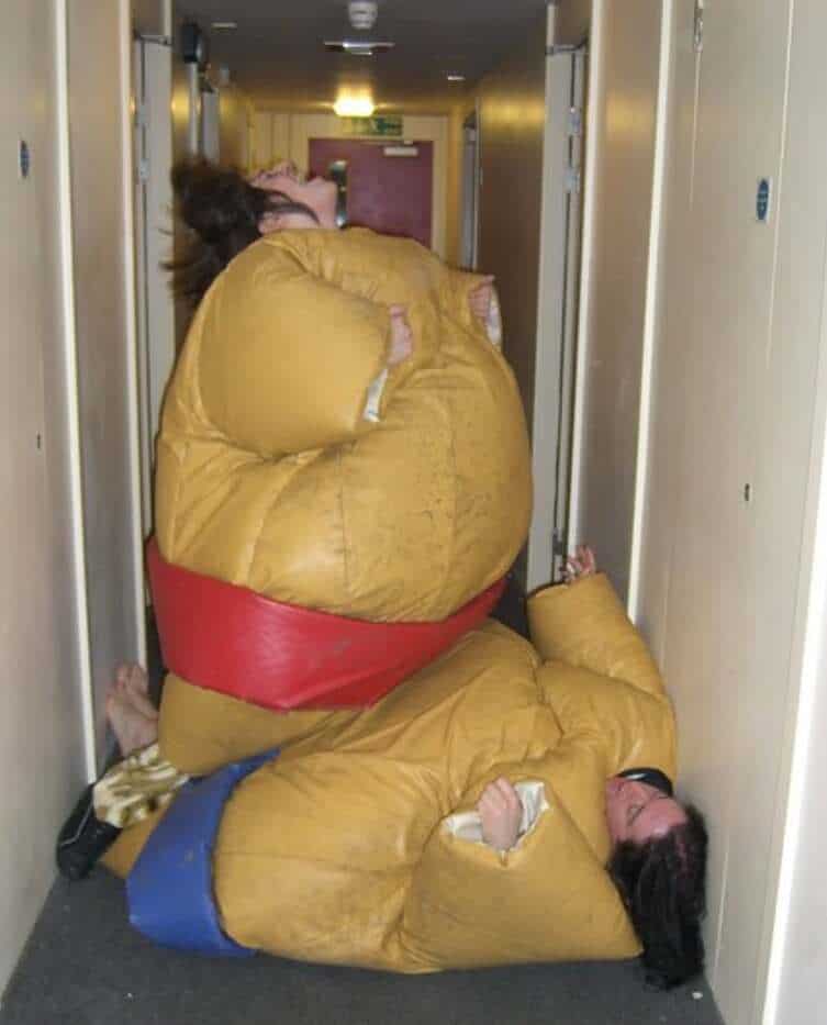 Two people in oversized costumes are stacked in a narrow hallway.