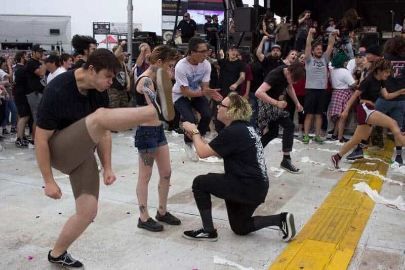 People at a concert or festival, some with legs raised, others dancing or taking photos.