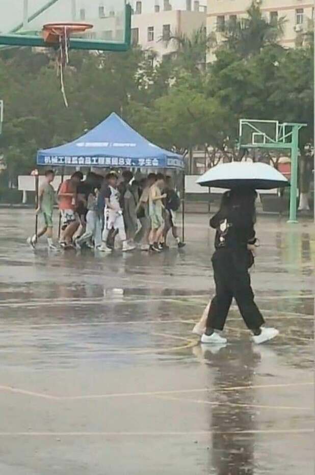 People walking on a wet basketball court under a blue tent and an umbrella.