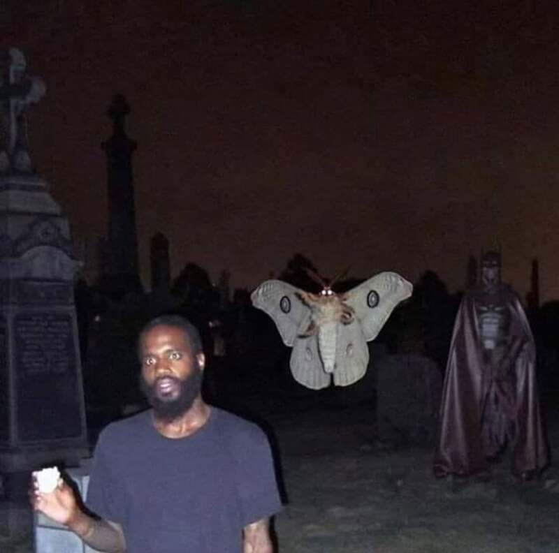 Man holding a piece of paper with a giant moth and a person in a cape in a graveyard at night.