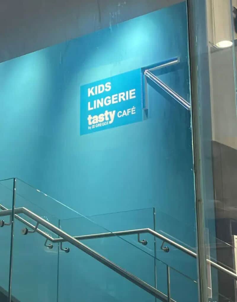 Sign for kids lingerie at Tasty Café by Greggs with a staircase below.