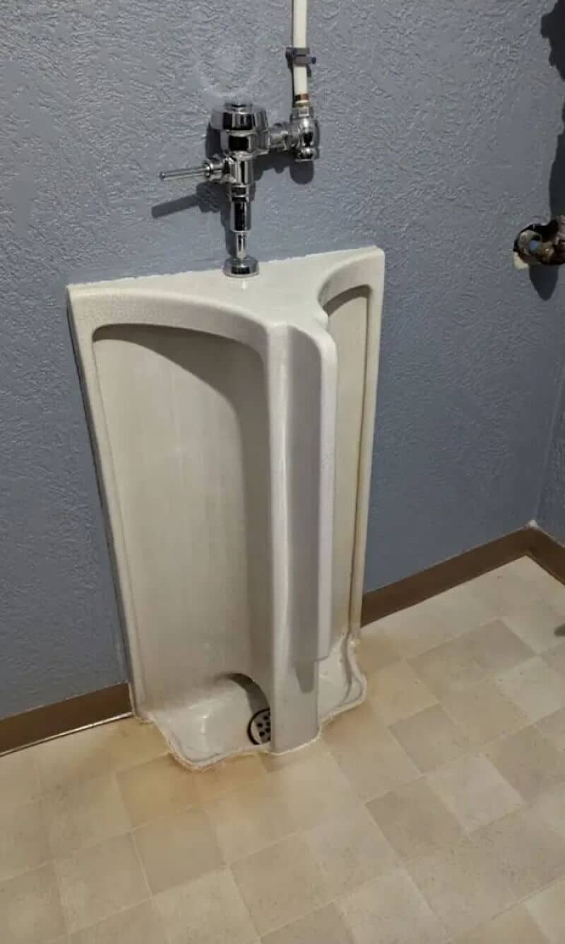 A urinal with a pipe attached to the top, mounted on a wall.