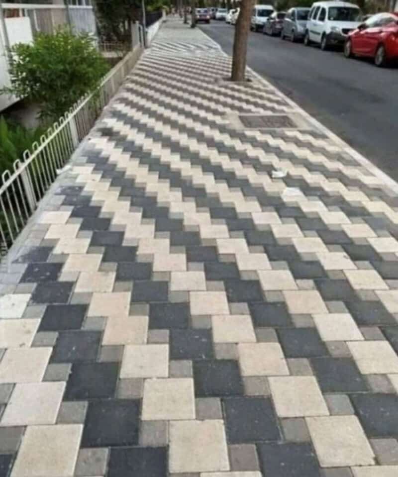 Sidewalk with a pattern of black and white tiles and a tree in the middle.