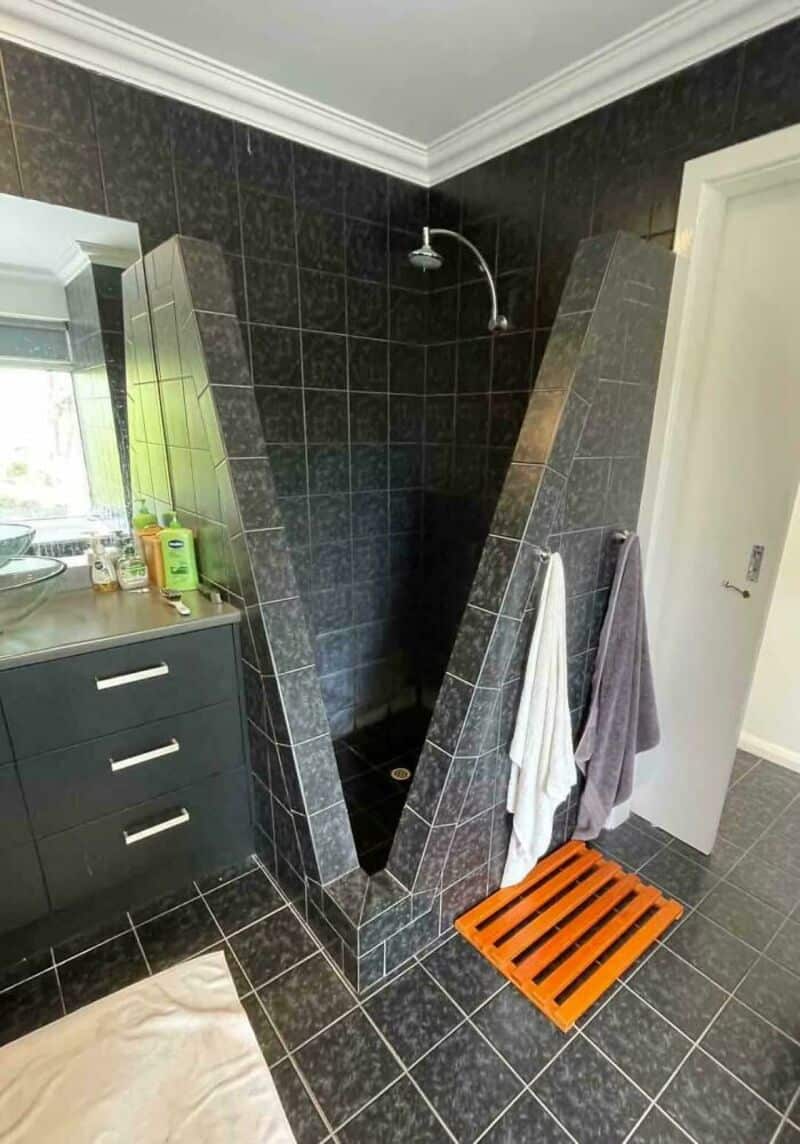 Unique black tiled shower with angled walls in a bathroom.