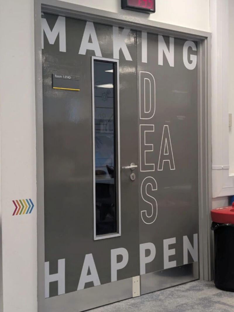 Door with text 'MAKING IDEAS HAPPEN' and 'DES' vertically on the right side.
