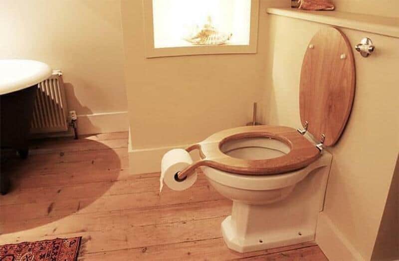 Toilet with a wooden seat and a roll of toilet paper on the lid.