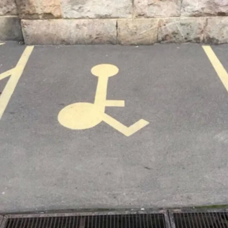 Parking space with a wheelchair symbol, but the symbol is poorly painted and distorted.