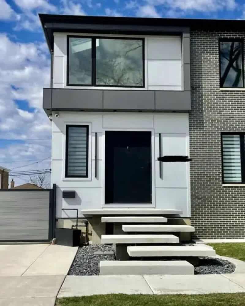Modern house with a staircase leading to the front door, with a large window above.