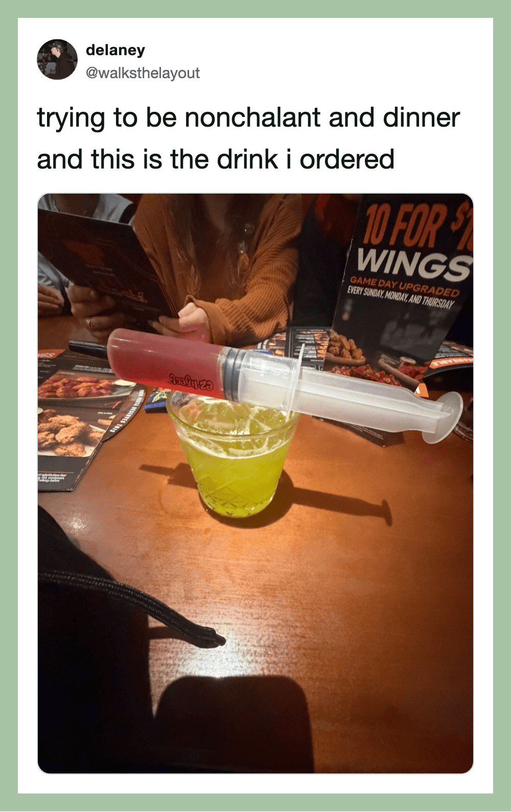 A drink in a glass with a syringe on top, at a restaurant table.