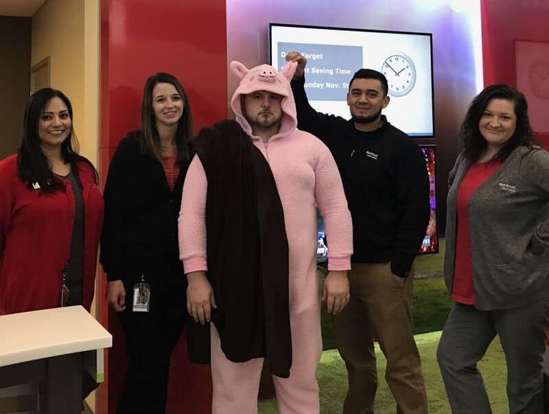 Group of five people posing indoors; one person in a pink pig onesie costume center, others in red/黑.