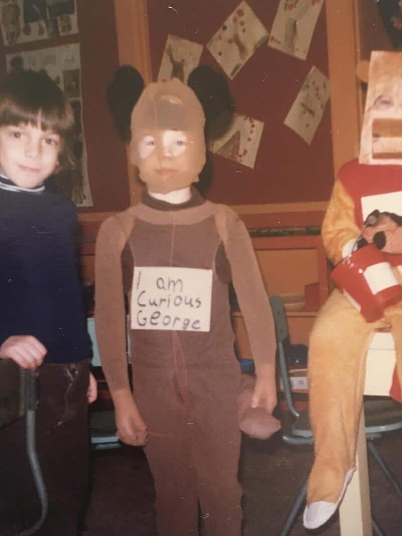Child in brown costume with sign reading 'I am curious George' and a masked face; other kids in the.